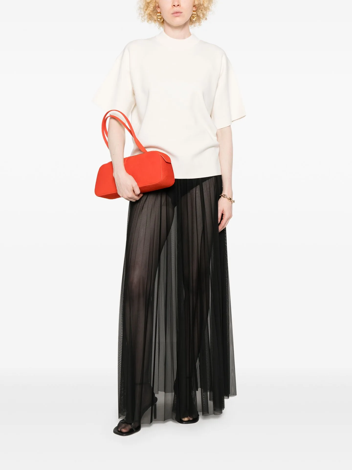 Cream knit top with a red shoulder bag and a sheer black pleated maxi skirt