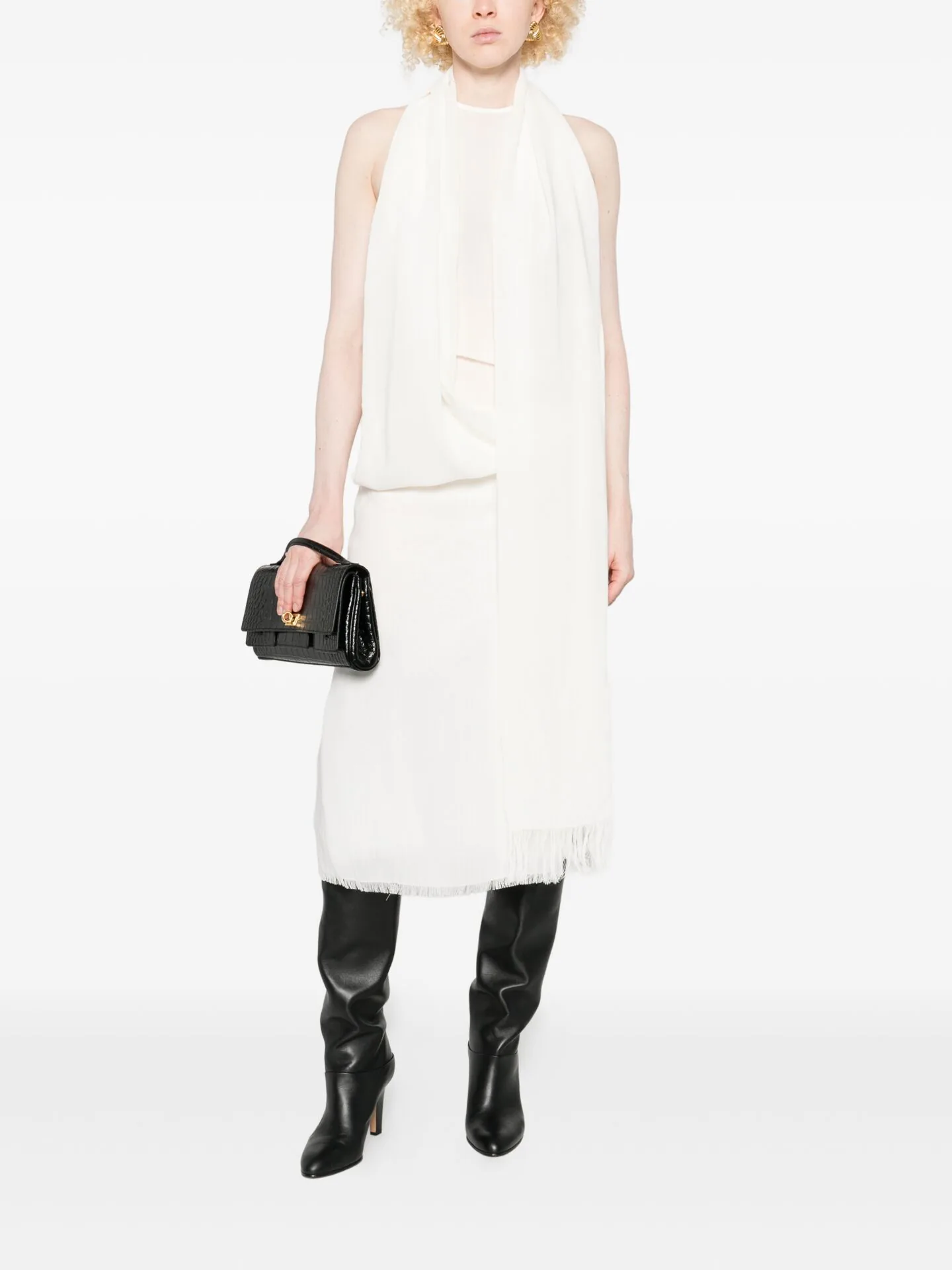 White sleeveless dress with a draped scarf, black knee-high boots and a small black bag