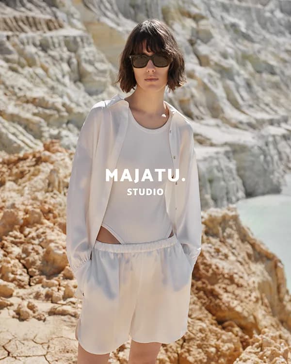 Model in a sheer white shirt and shorts on pale rock, MAJATU. Studio logo overlaid