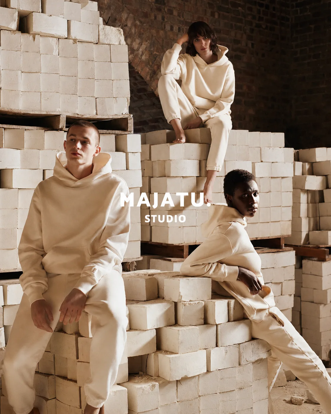 Three models in cream loungewear seated among stacked pale bricks