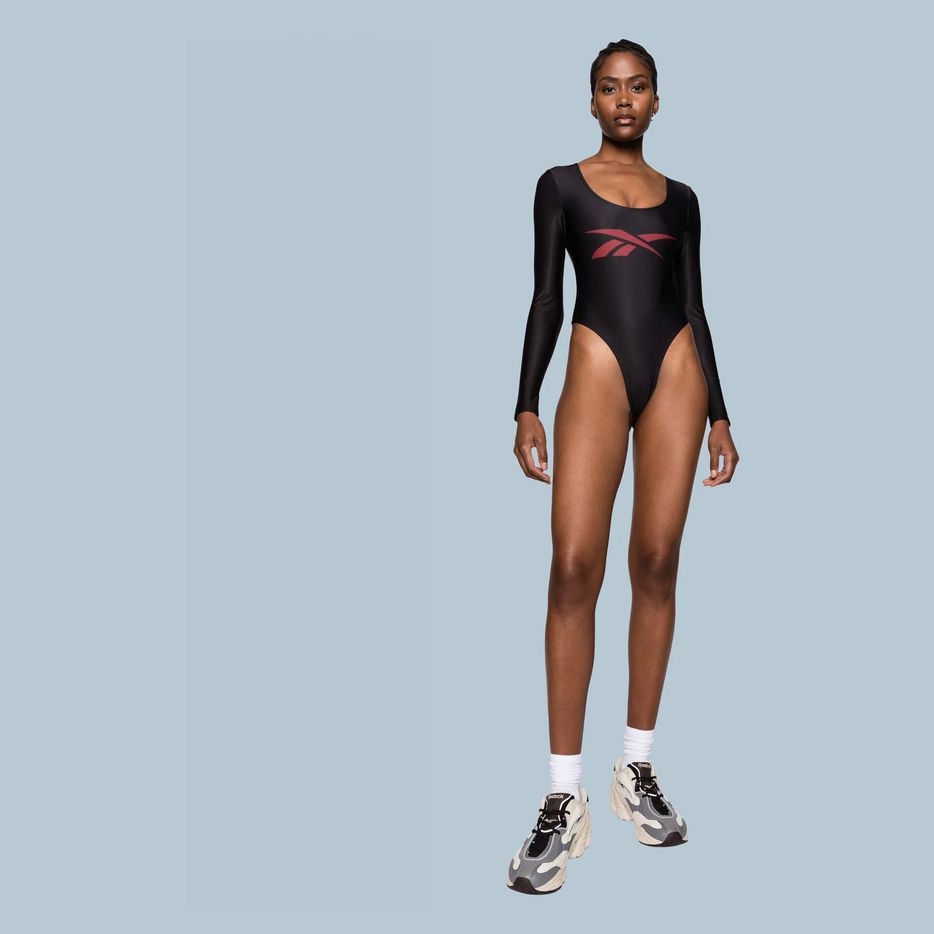 Model in a black long-sleeved Reebok bodysuit and chunky trainers