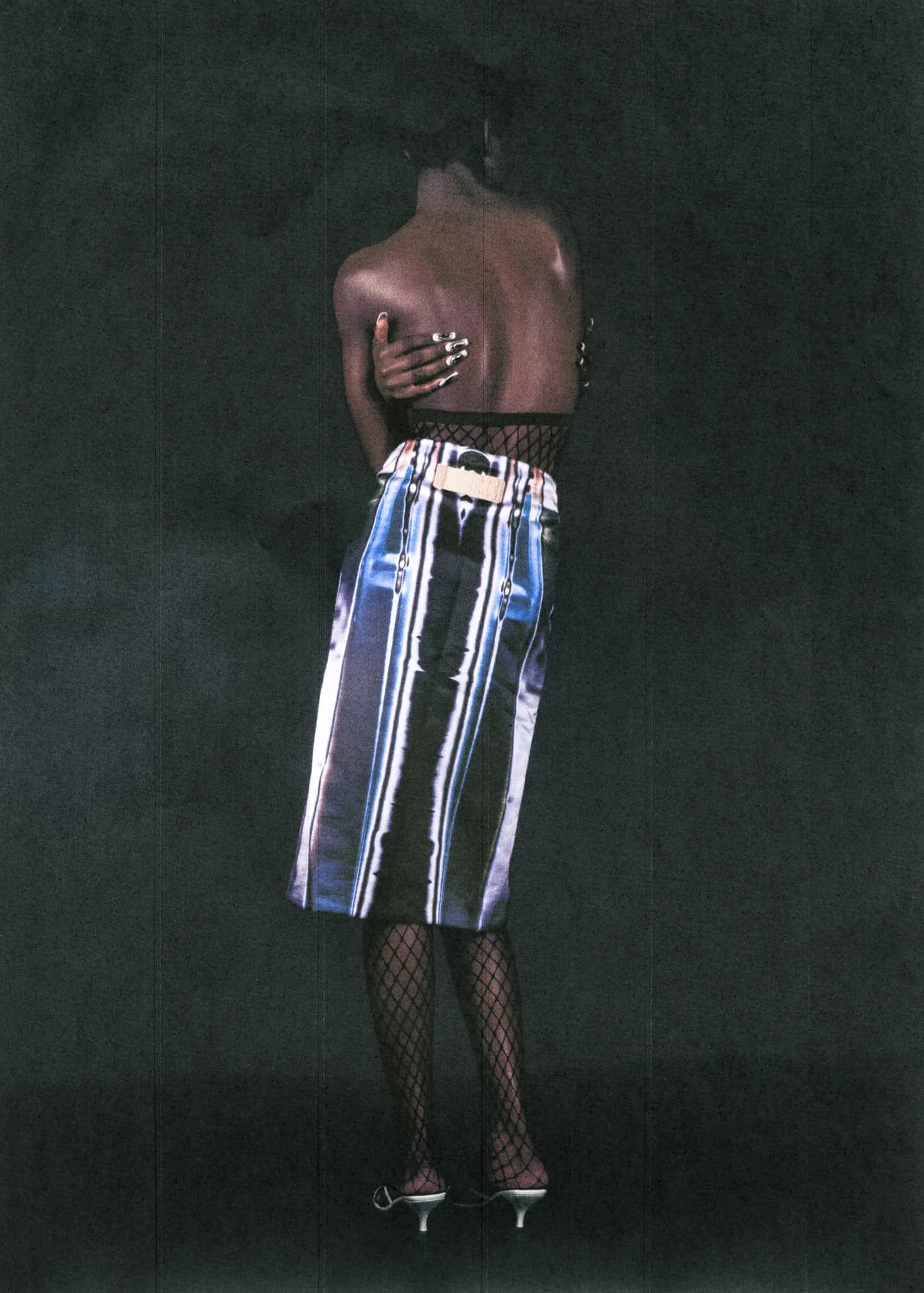 Back view of a model in an iridescent striped skirt and fishnets, one hand across the shoulder