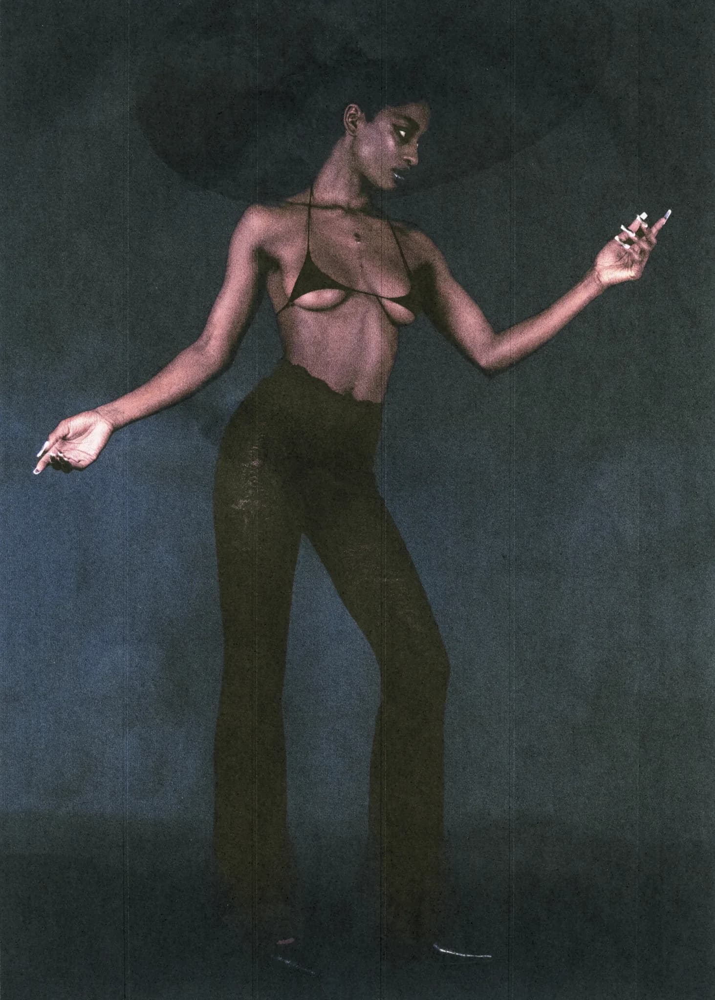 Model in a wide-brimmed hat, halter top and dark trousers, arms outstretched