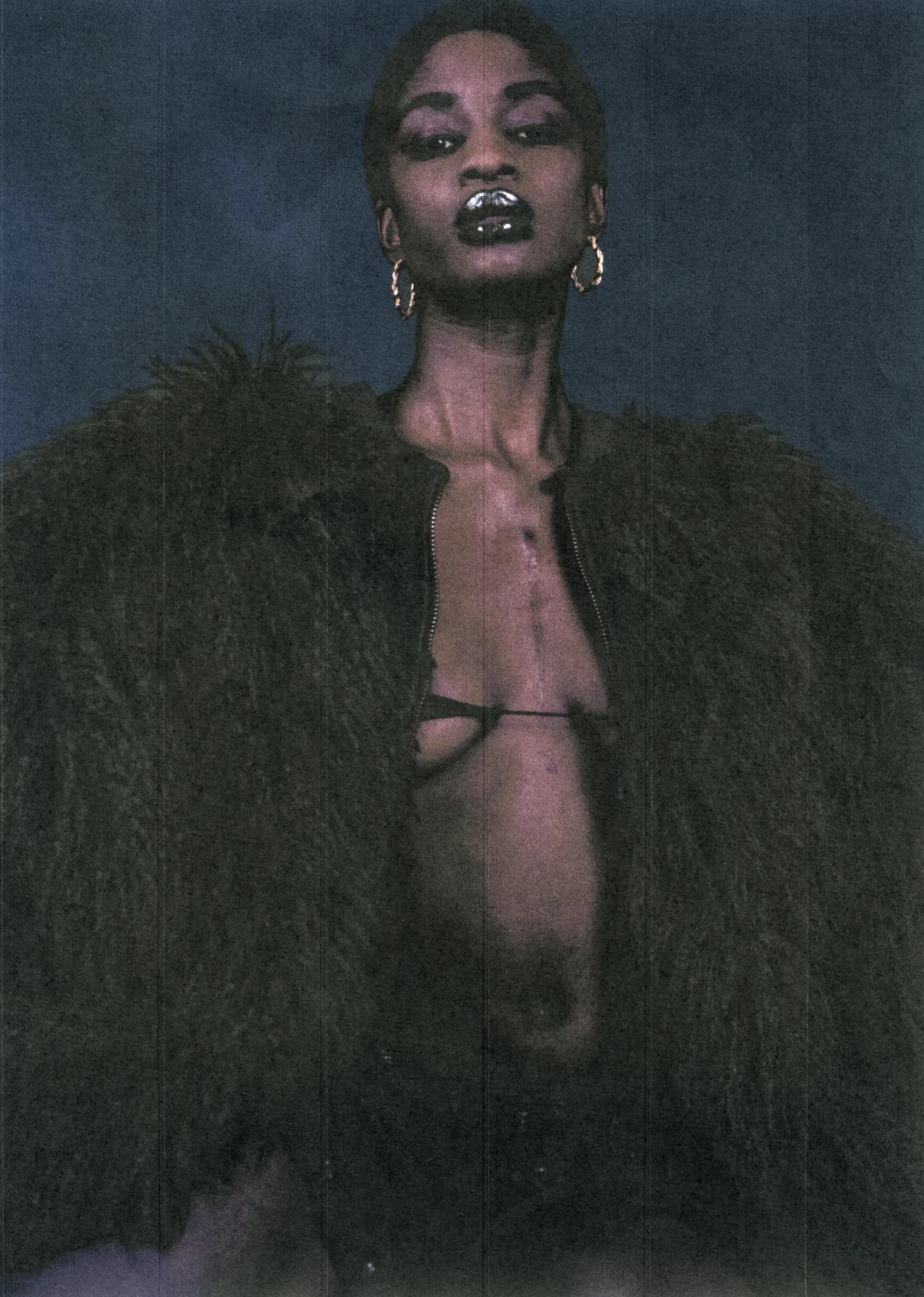 Model in an open black fur coat and fine chain harness, looking to camera