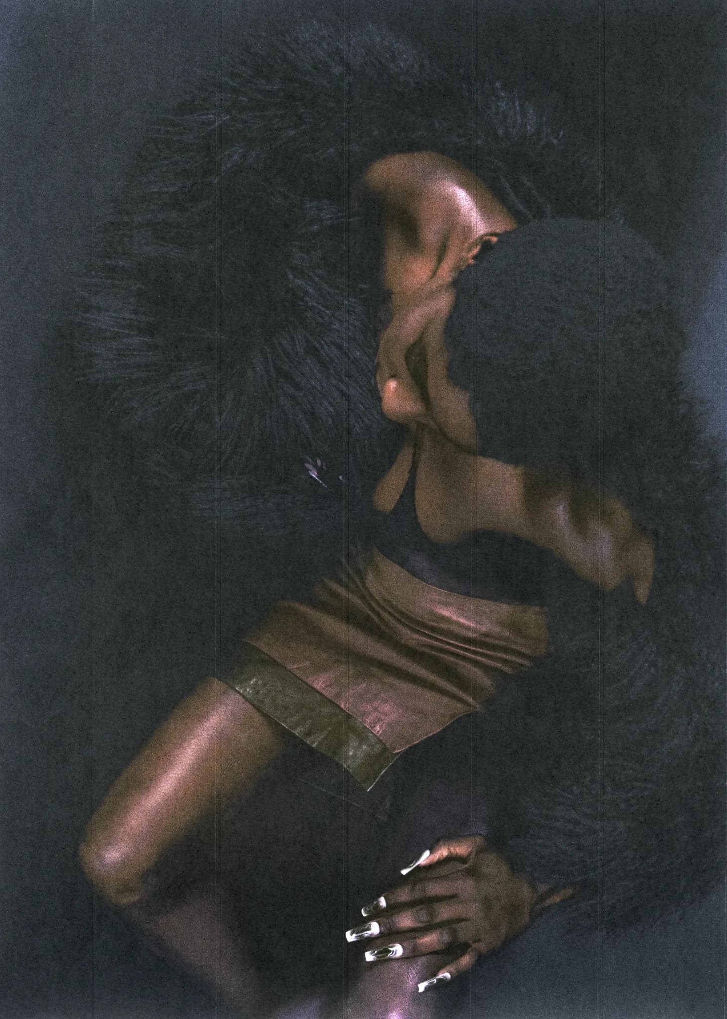 Model arched backwards in a bronze bandeau and shorts, black fur framing the pose against a dark backdrop