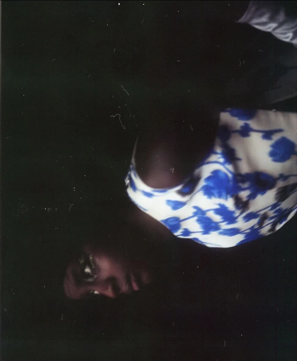 Figure lying in a blue and white floral dress, face turned to camera in low light