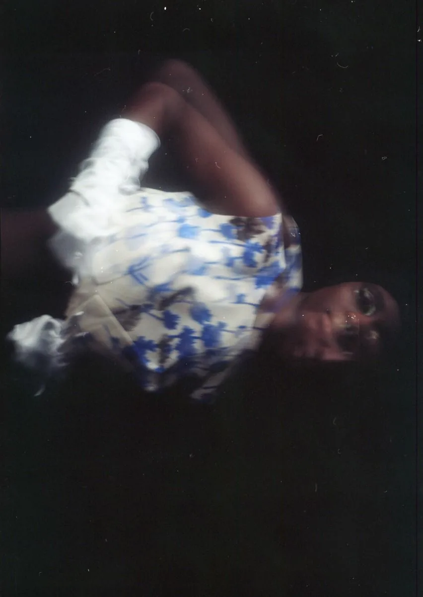 Blurred figure in a blue and white floral dress against near-darkness, shot on film
