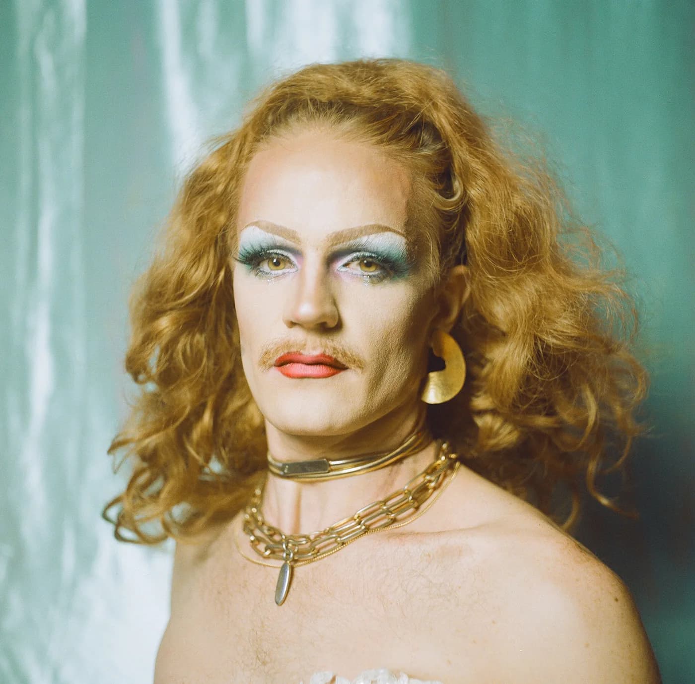 Close portrait of a performer with blue eyeshadow, gold chain and hoop earrings