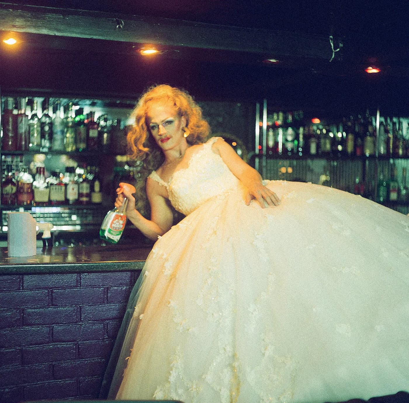 Performer in a full cream tulle gown holding a bottle behind a bar