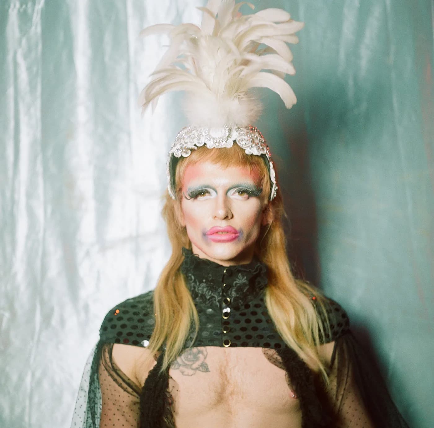 Performer in a feathered headdress and sheer black cape against a pale curtain